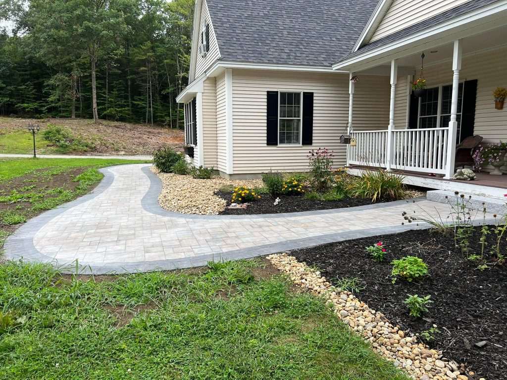 Curving paver walkway leading to the front porch of a home with planted beds alongside